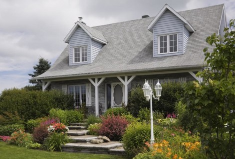Facade of old grey nuanced brick with white trim cottage style Canadiana home with dormer windows