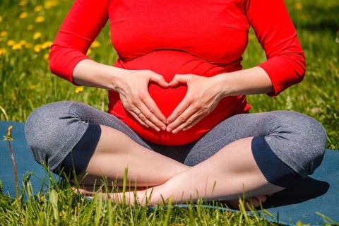 Pregnancy yoga exercise, pregnant woman doing asana Sukhasana easy yoga pose showing heart symbol