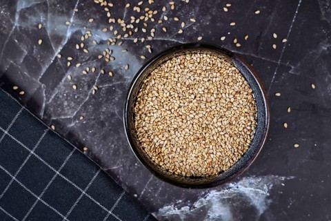 Top view of white sesame seeds in bowl on dark background