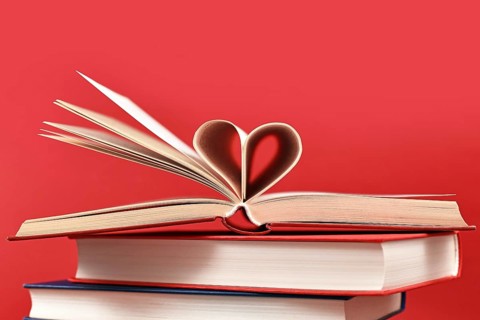 Pages folded into heart shape on stack of old hardcover books on red background