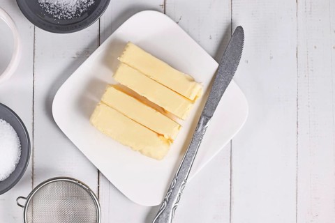 Slices of butter for baking next to knife on white plate on wooden table