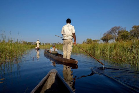 Tourists in a mokoro or dugout boat on safari in swamp area, Gomoti Plains Camp, Gomoti Concession