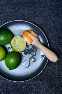 Limes with citrus squeezer on plate, halved
