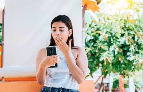 Girl with cell phone with a surprised face leaning on a wall. Young woman with the cell phone with