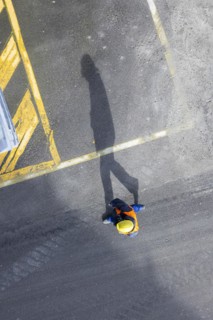 A construction worker in a hard hat walks over tarmac. He casts a long shadow. Stuttgart,