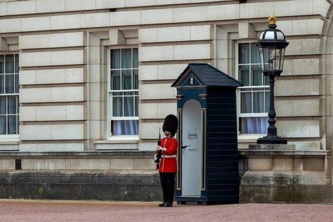 A guard in red uniform stands in front of a sentry box next to a lantern at Buckingham Palace,
