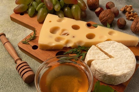 Cheese with big holes, emmental, maasdam, brie cheese, on a cutting board, with grapes and honey,