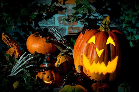 Halloween pumpkin surrounded by spiders, decorative pumpkins and bone hands in a gloomy setting