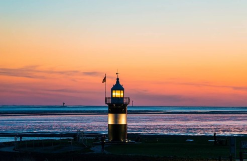 Black and white lighthouse, called 'Kleiner Preuße', lighthouse and boat at sunset on the coast,
