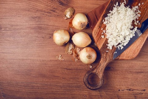 Finely chopped onion on a chopping board with a knife, wooden table, top view, no people
