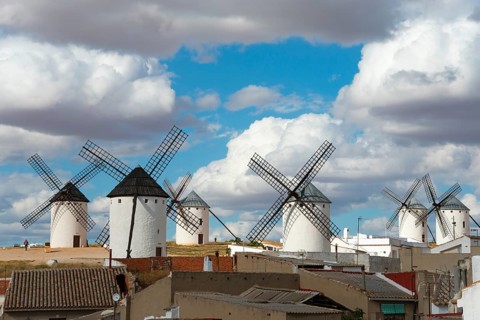 Several mills in a rural area, with old buildings in the foreground and a cloudy sky above, Campo