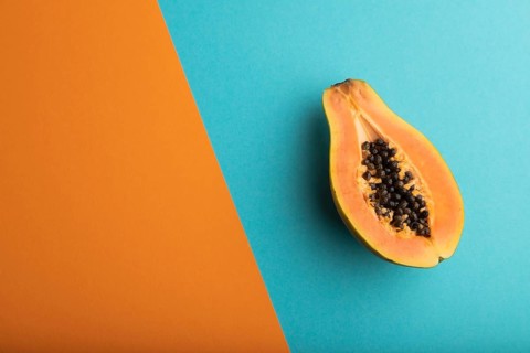 Ripe cut papaya on orange and blue pastel background. Top view, flat lay, copy space. Tropical,