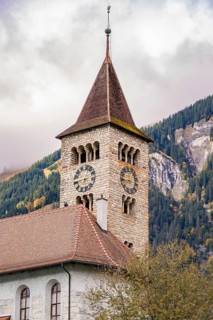 A traditional stone church tower in front of an autumnal wooded mountain, Lake Brienz, Switzerland,