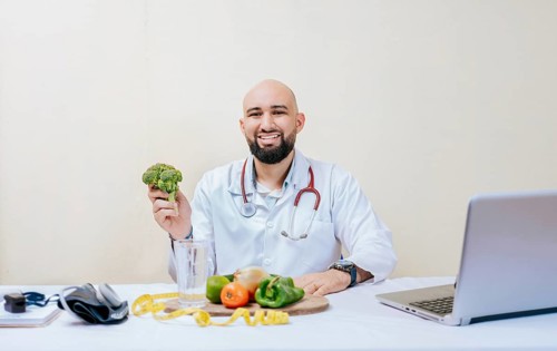 Portrait of smiling nutritionist holding a broccoli. Smiling nutritionist doctor at his desk