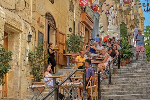 Tourists enjoy a break on the steps of the St. Lucia Street, Valletta, Malta, Europe