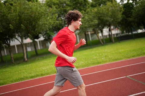 Side view of a young caucasian man running with tired expression along a running track
