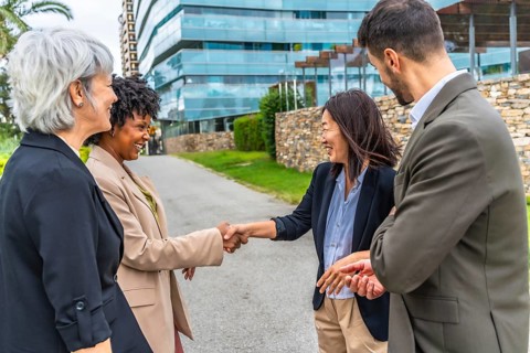 Multi-ethnic businesswomen shaking hands during outdoor meeting next to business colleagues in the