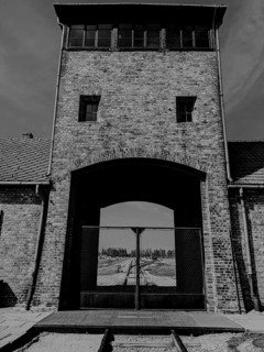 A historic brick building with a watchtower and gate, featuring rail tracks in front.