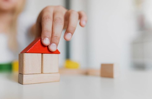 Little child girl of preschooler age playing wooden building blocks at home or kindergarten. Kid is