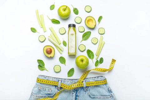 Green fruit, vegetables, smoothie falling into jeans and yellow measuring tape instead of belt on