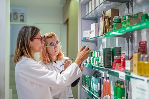 Two pharmacists in white coats and glasses check and examine products on a pharmacy shelf