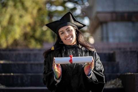 Transgender woman recent graduated, dressed in cap and gown, showing off his degree celebrating