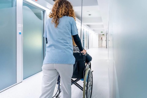 Rear view of a nurse pushing wheelchair with woman along the corridor of an hospital