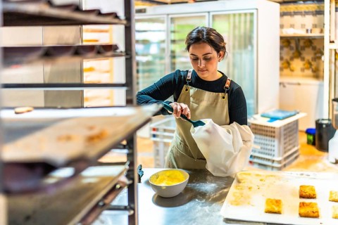 Female latin artisan baker filling a piping bag to decorate pastries in the workshop kitchen of a
