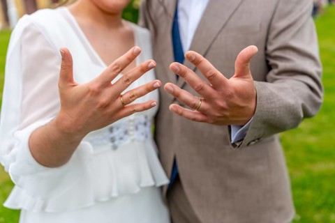 A couple is posing for a picture with their wedding rings. The man is wearing a suit and tie, while