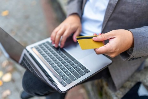Close-up of a caucasian man shopping online using laptop and credit card sitting on city bench