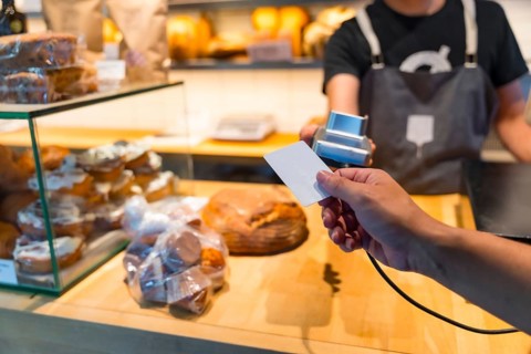 Customer in the bakery shop buying an artisan bread from the baker in the workshop, paying with the