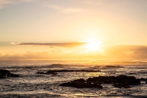 Sunrise over the sea with gentle waves. Sandy beach with lava rocks and blue water alternating with