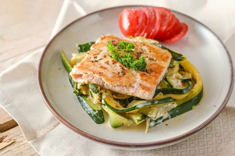 Fried wild salmon with parsley garnish on zucchini vegetables and fresh tomato on a light plate,