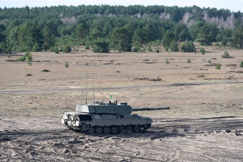 A Leopard 1 tank drives through a sandy landscape with pine forests in the background, Germany,