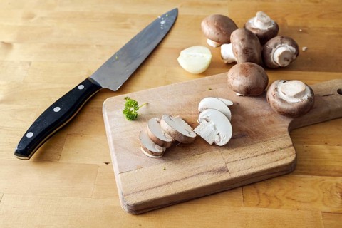 Mushrooms whole and sliced on a wooden cutting board and a kitchen knife, preparation for cooking a