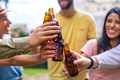 Multi-ethnic group of friends partying in a city park with beers. toasting with the bottles