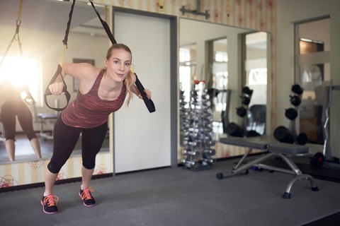 Young fit blond woman exercising with suspension bands in a modern gym in the morning