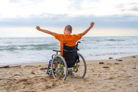 Disabled person on his back in a wheelchair on the beach with open arms enjoying the freedom