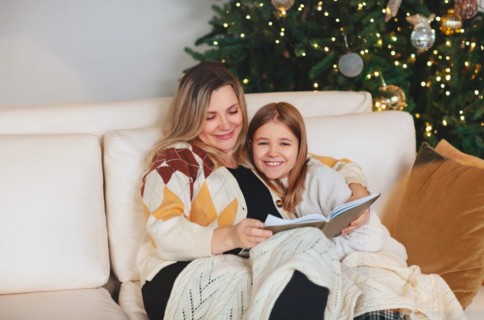 Happy family grandmother and little girl daughter sitting together on sofa and reading book while