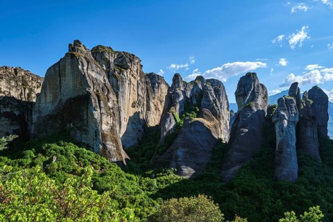 Midday view of Meteora rocks, sedimentary cliffs among bright spring greenery of valley. Sunshine,