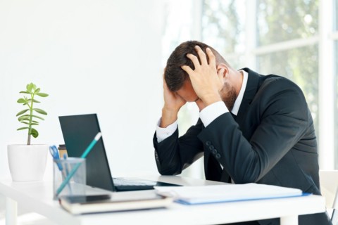 Stressed tired businessman sitting at the desk in creative office. Man suffer from headache,
