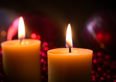 2 lit candles in front of Christmas decorations
