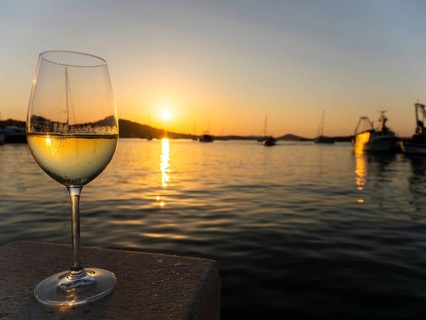 Sunset shimmering through a glass of white wine, evening mood in the harbour, boats and sailing