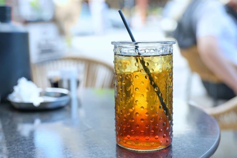 Refreshing iced tea with lemon syrup and a drinking straw in a glass in a street cafe in the