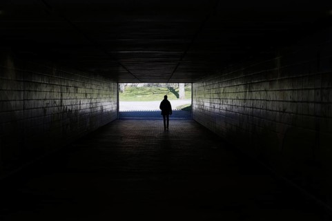 silhouette of a person walking through a dark underpass symbolizing light at the end of the tunnel