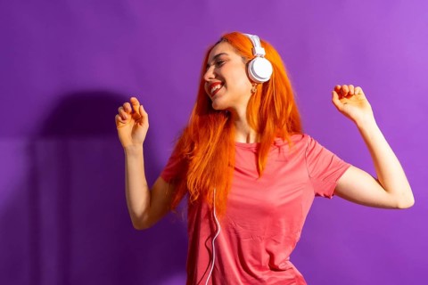 Redhead woman in studio photography dancing on a purple background, with a hard light