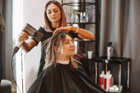 Happy woman with stylist making hairdo at salon. Competent female hairdresser deciding what to do