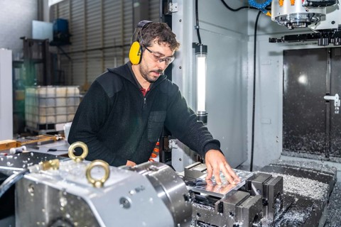 Manual worker with protective goggles and headphones using a milling cnc modern machine