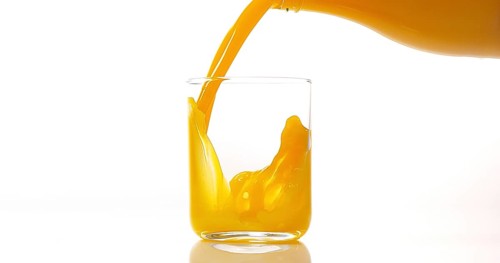 Orange Juice being poured into Glass against White Background