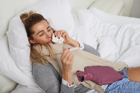 Sick woman with a miserable expression taking her temperature as she lies in bed suffering from a